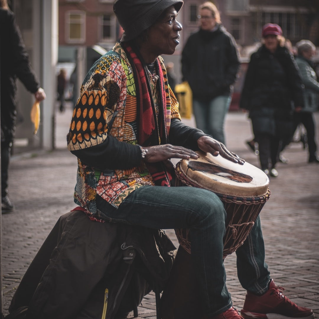 Teranga Africa/Choose Senegal musician playing a hand-carved wooden djembe drum with goatskin head on a city street