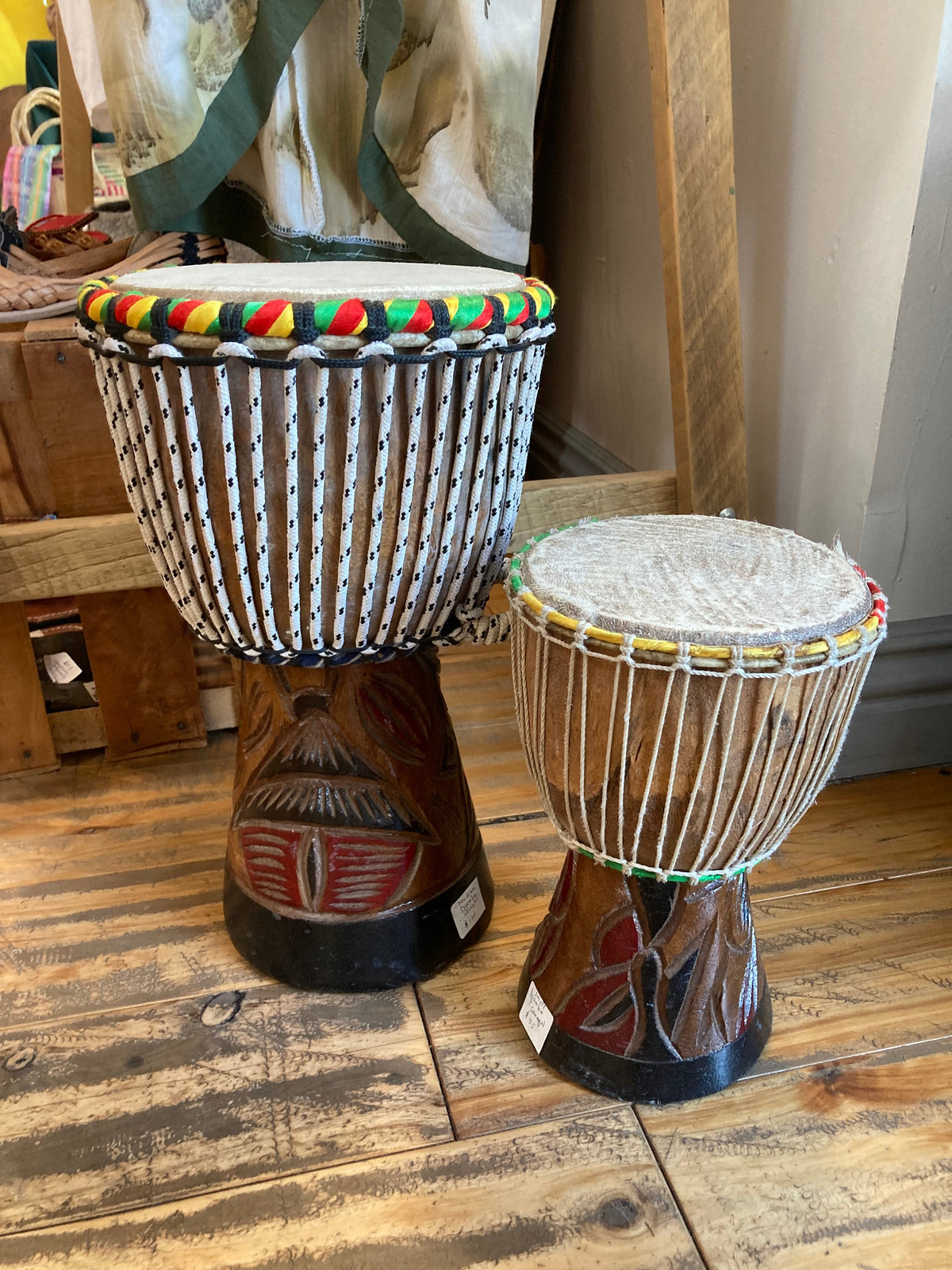 Two Teranga Africa/Choose Senegal hand-carved wooden djembe drums with goatskin heads and colorful braided cord trim.